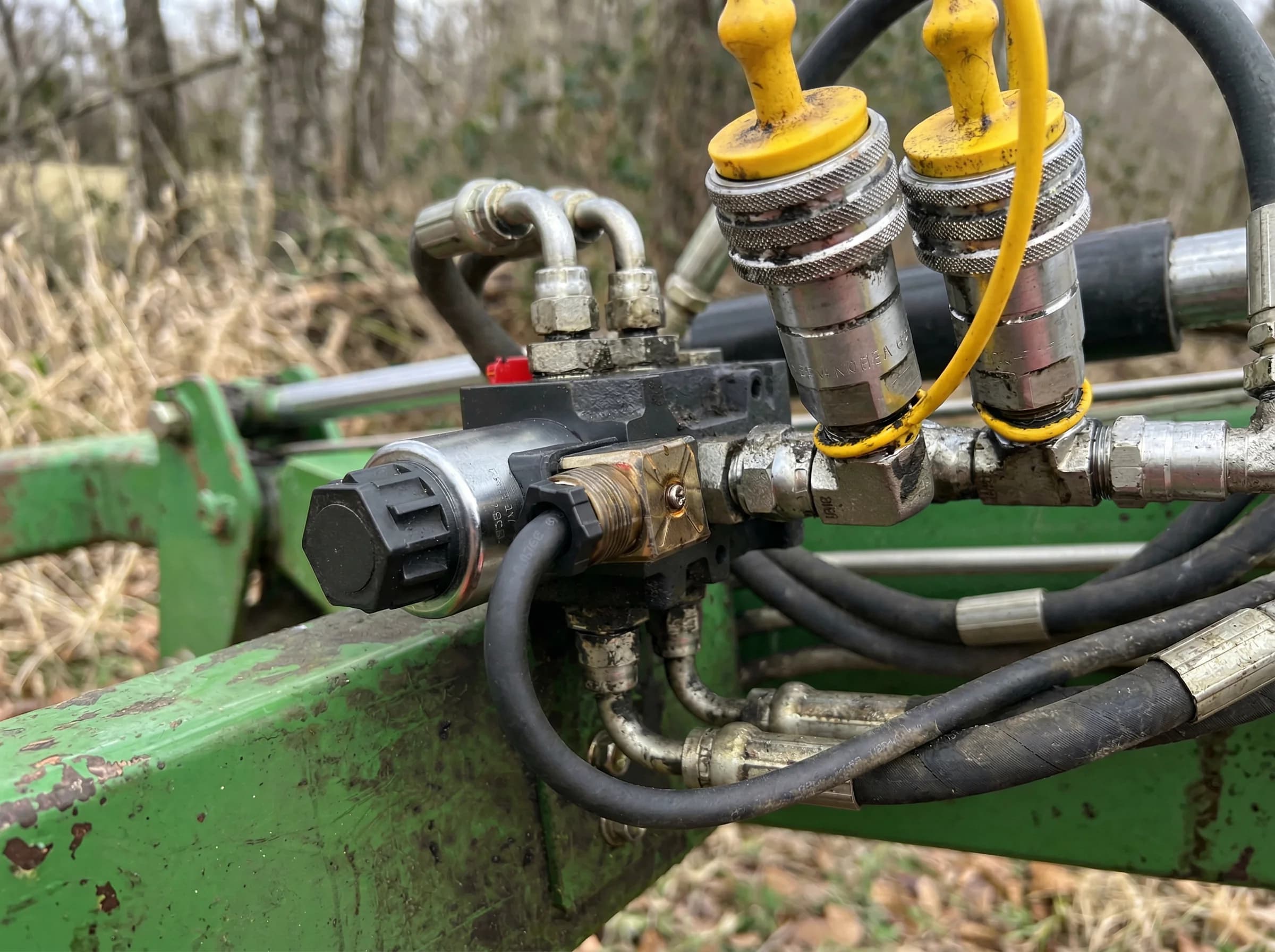 12V hydraulic solenoid valve block mounted on a green agricultural implement with rubber hydraulic hoses and quick-couplers