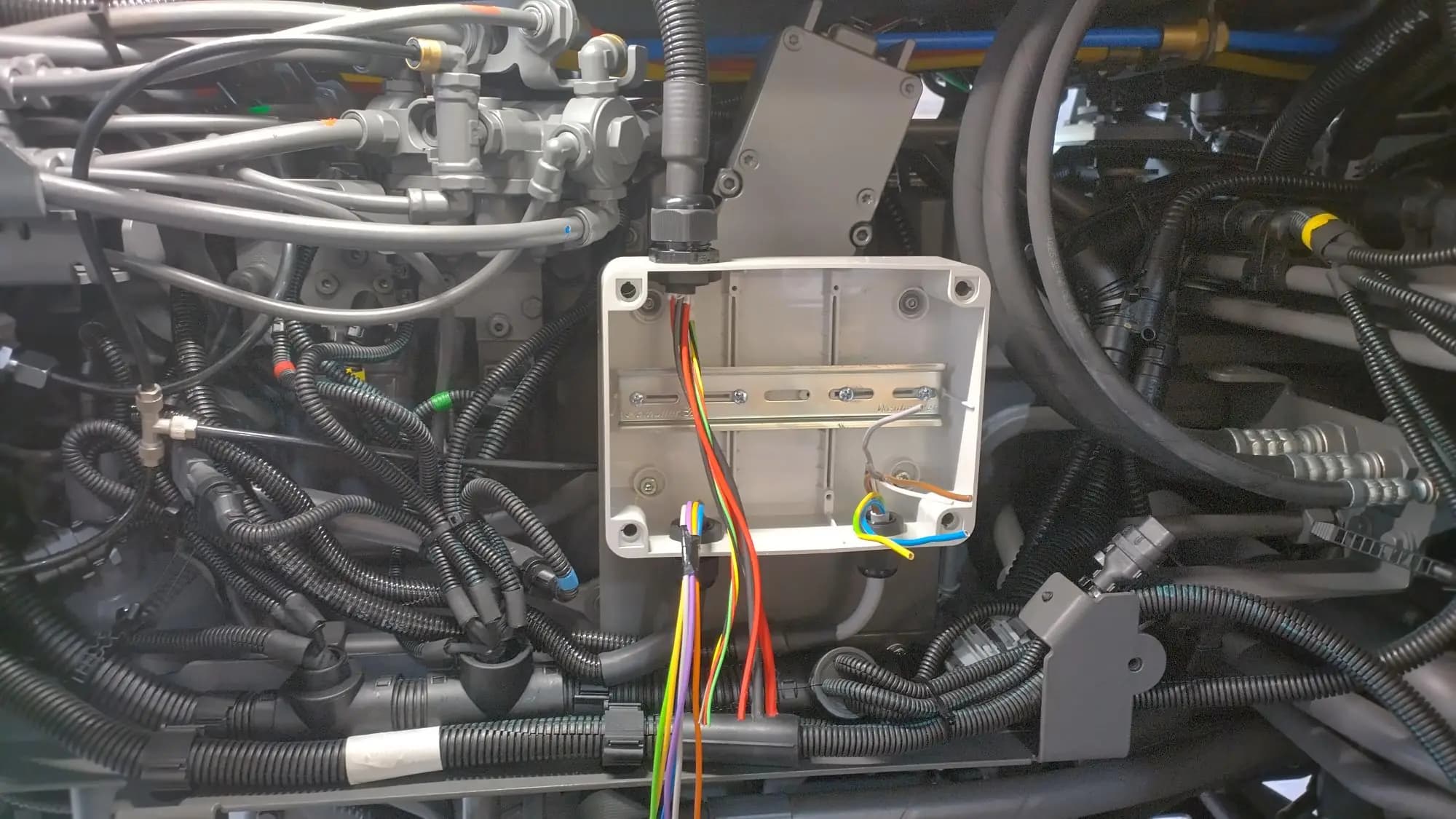 The empty enclosure early in the install: bare DIN rail, coloured relay leads and ISOBUS supply already routed in through the top gland