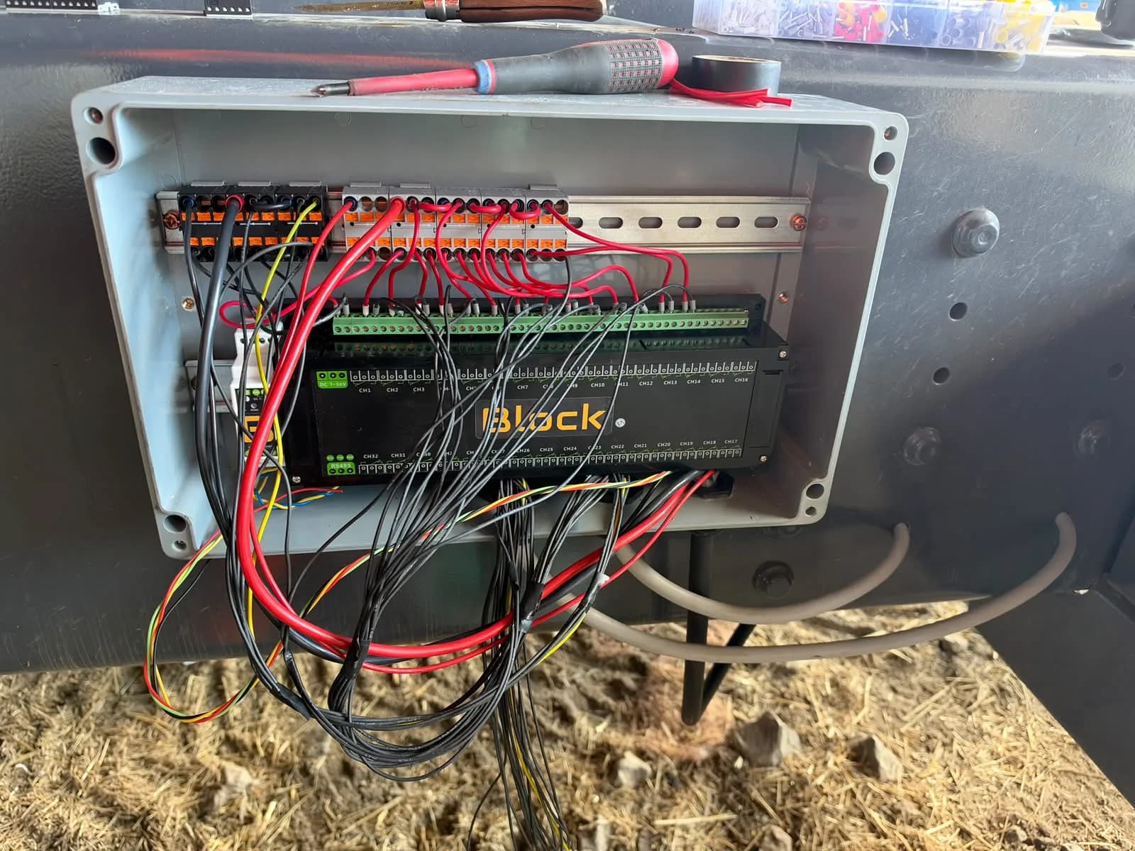 The enclosure mid-wiring: push-in terminal blocks fitted above the module, red supply jumpers going on, black load leads routed down to the channel terminals
