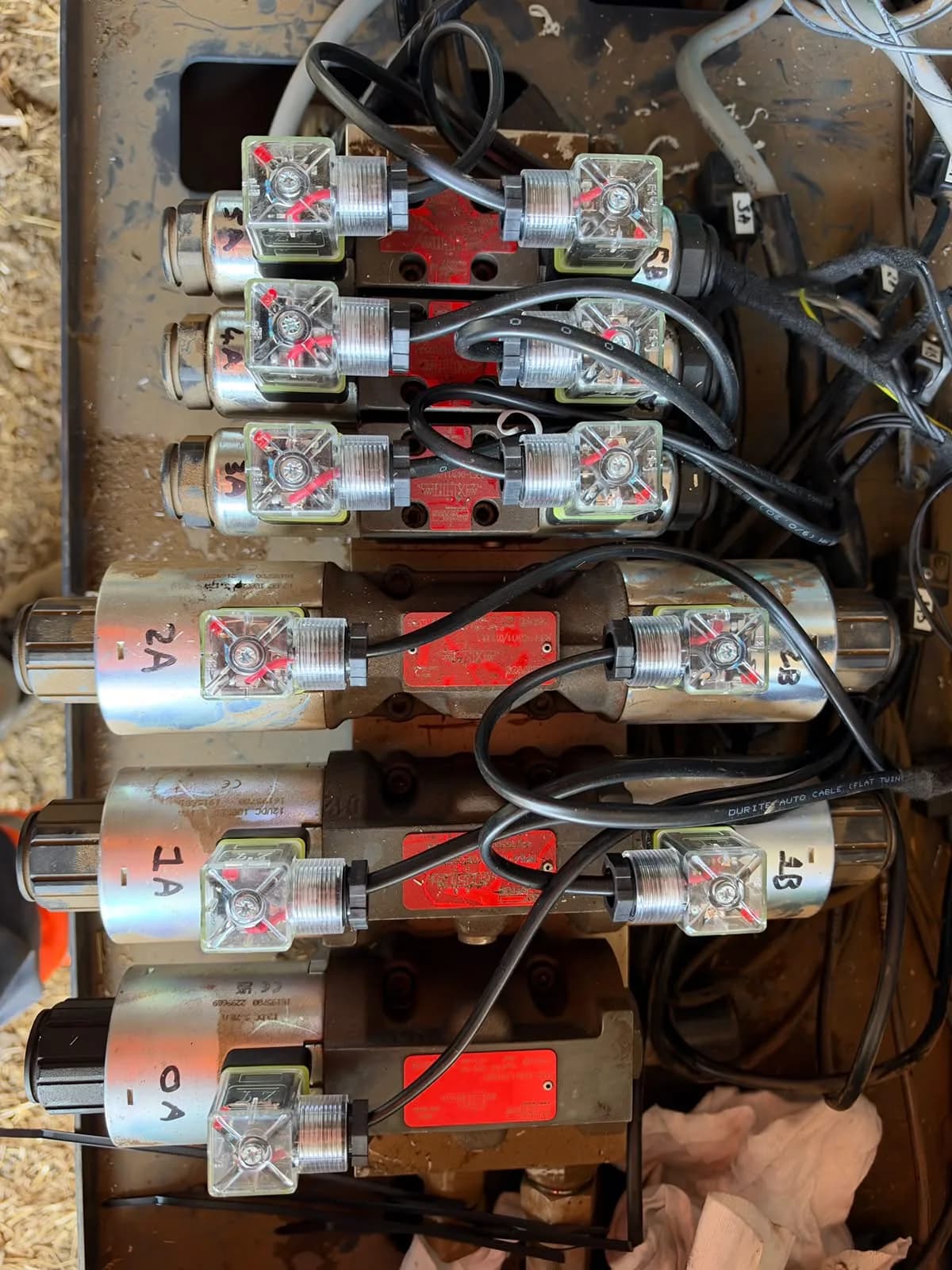 The hook-lift trailer’s hydraulic valve bank laid out on the chassis: six solenoid valves, each coil connector marked by hand with its section and side, 0A to 5B