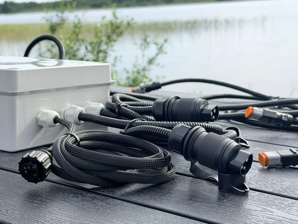 Closed grey enclosure of an 8-channel ISOBUS Block on a deck beside its braided cab harness, two round ISOBUS plugs and Deutsch connectors
